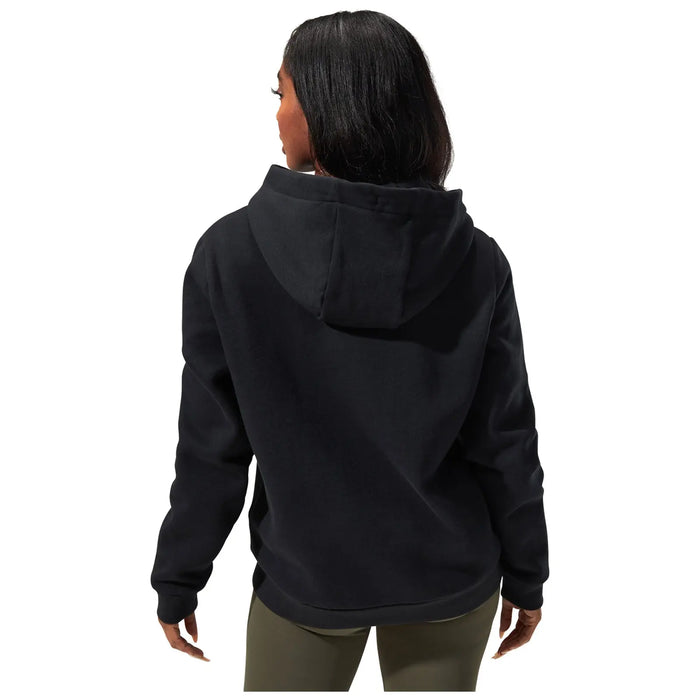 A person wearing a black hooded sweatshirt stands with their back facing the viewer their long hair cascades over the collar in a plain white background.